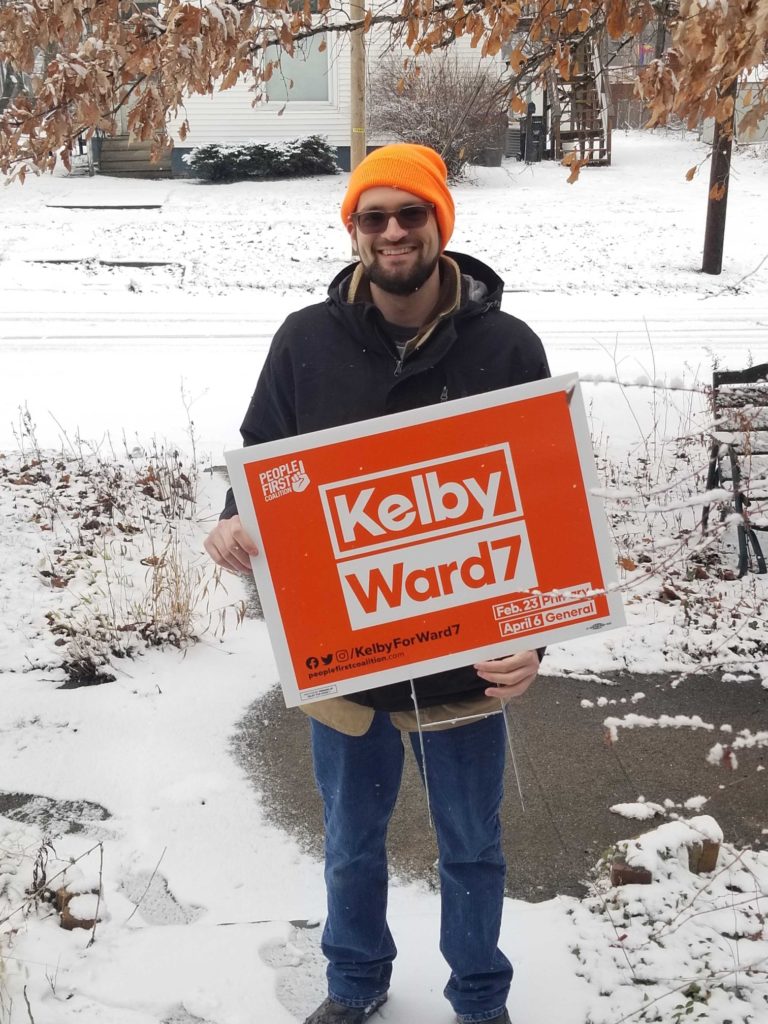 Kelby Cumpston holding a campaign sign for his Bloomington Election